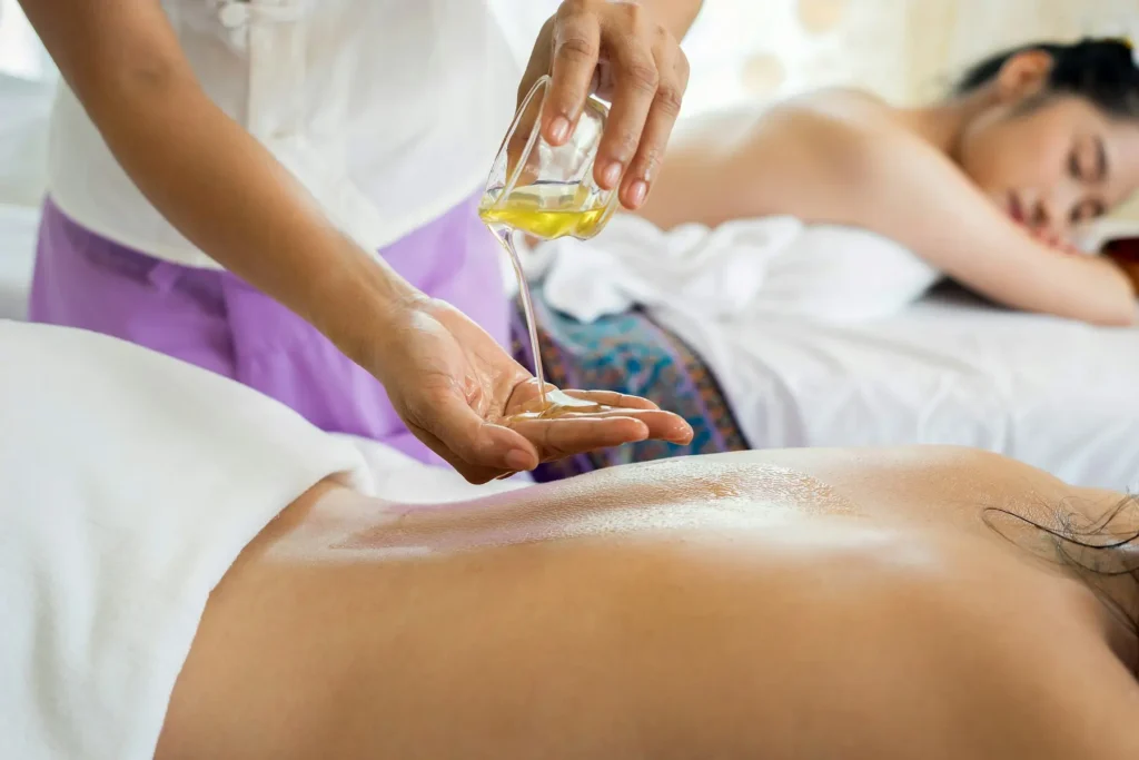 The image shows a close-up of a massage therapist's hands working on a client's back in warm, moody low-key lighting